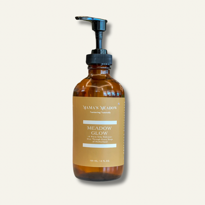 A clear glass bottle with a pump dispenser, labeled 'Meadow Glow - Body Oil'. The bottle is amber-colored and contains the product.