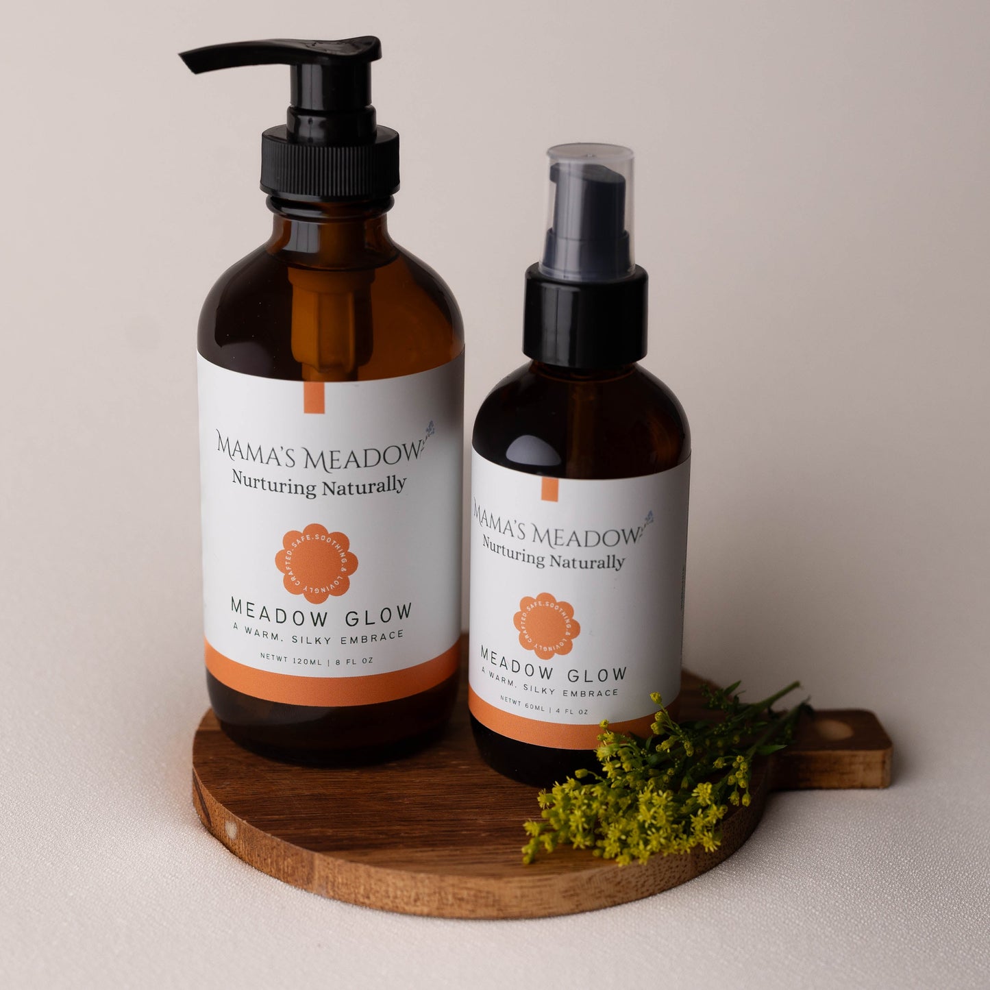 Two bottles of 'Mama's Meadow' products on a wooden board with a neutral background